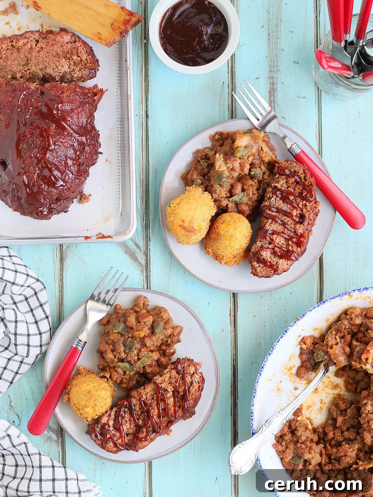 Sliced of meatloaf garnished with barbecue sauce with a side of baked beans and fried hush puppies.
