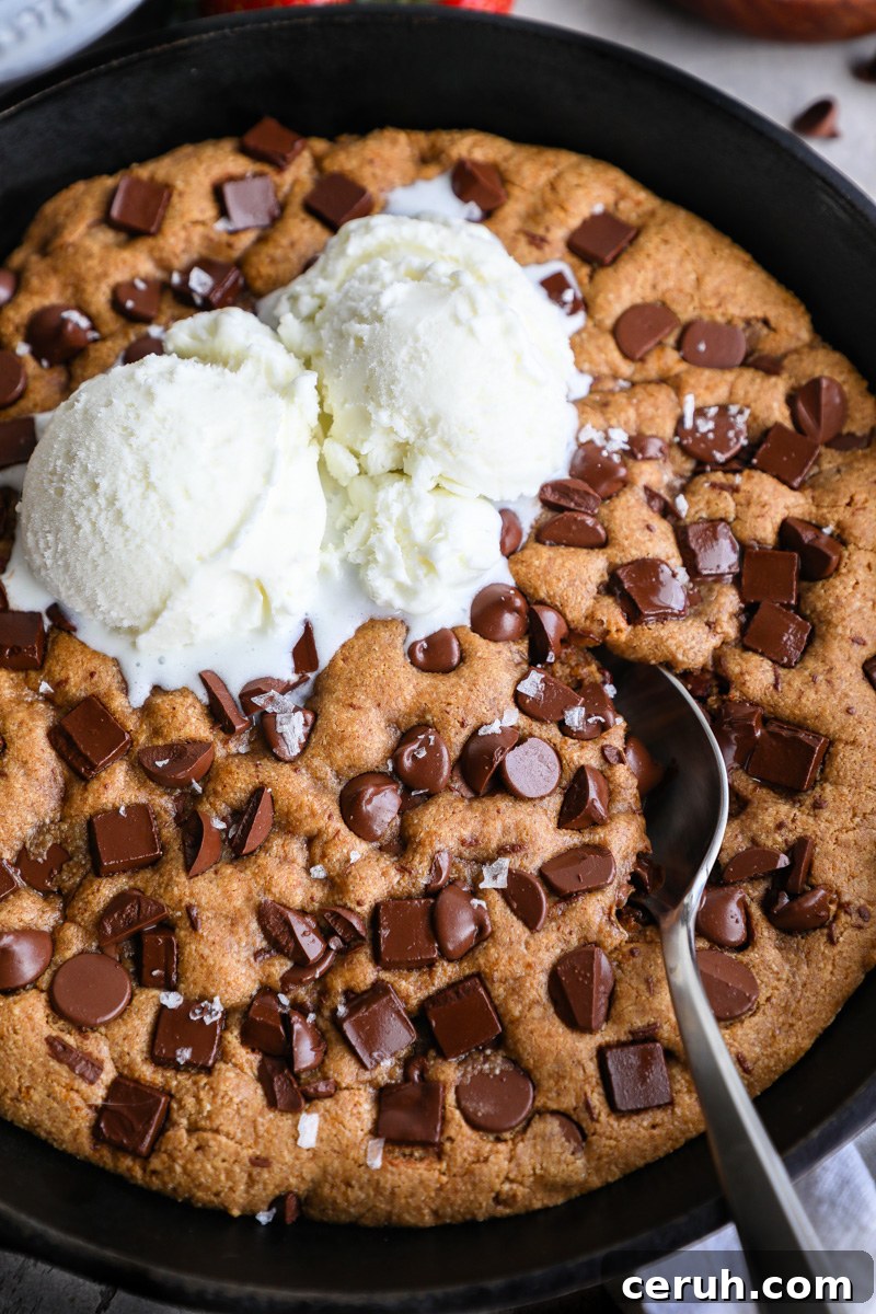 A close up photo of a skillet cookie baked in a cast iron skillet topped with vanilla ice cream