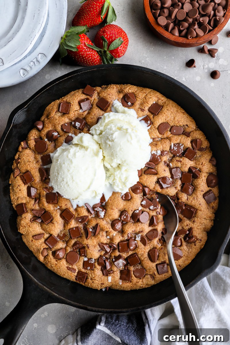 An almond butter chocolate chip skillet cookie sitting next to a bowl of chocolate chips and fresh strawberries