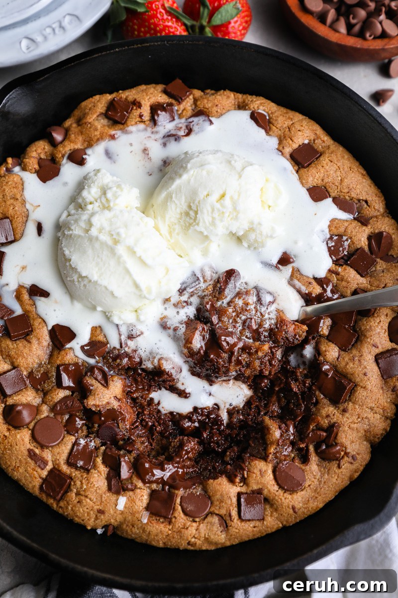 An almond butter skillet cookie topped with melted vanilla ice cream with a scoop taken out of the center