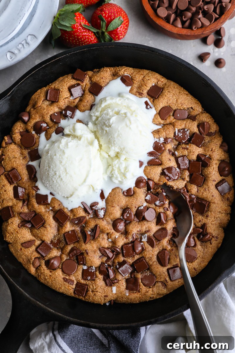An almond butter chocolate chip skillet cookie topped with 2 scoops of vanilla ice cream with a spoon digging into it