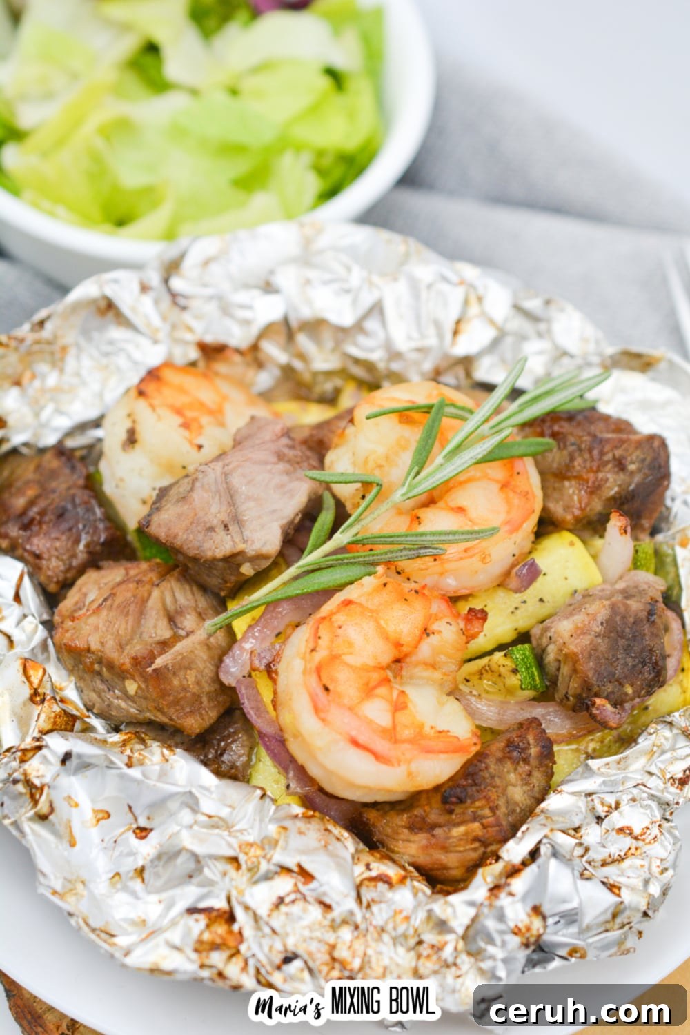 opened foil packet filled with steak, shrimp, and cooked vegetables.