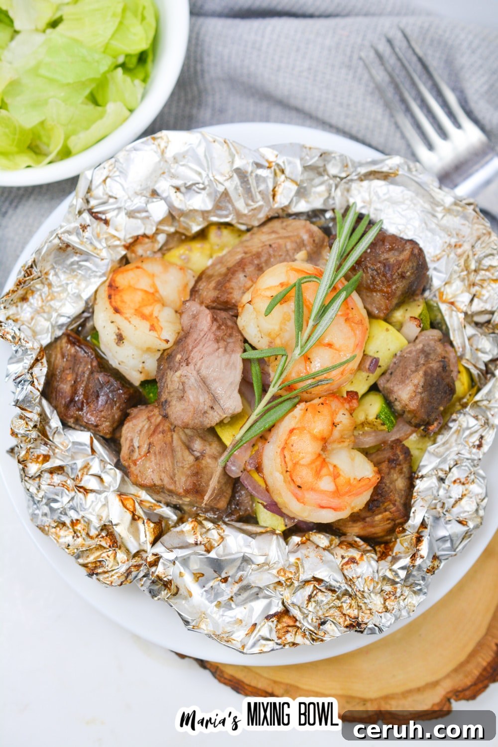 opened foil packet filled with steak, shrimp, and cooked vegetables.