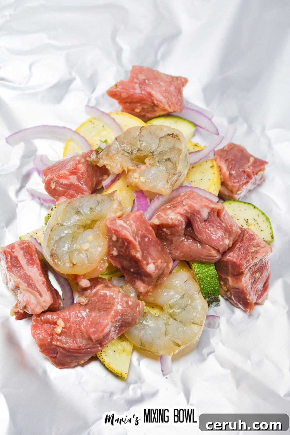 raw vegetables, raw steak, and raw shrimp being added to a foil packet.