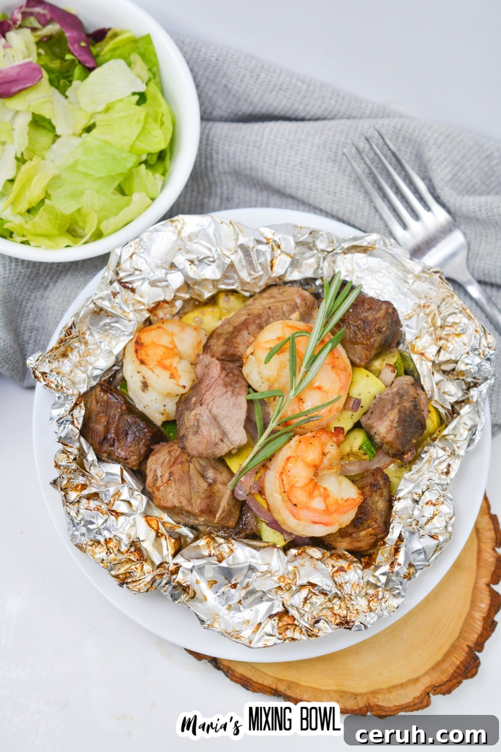opened foil packet filled with steak, shrimp, and cooked vegetables.