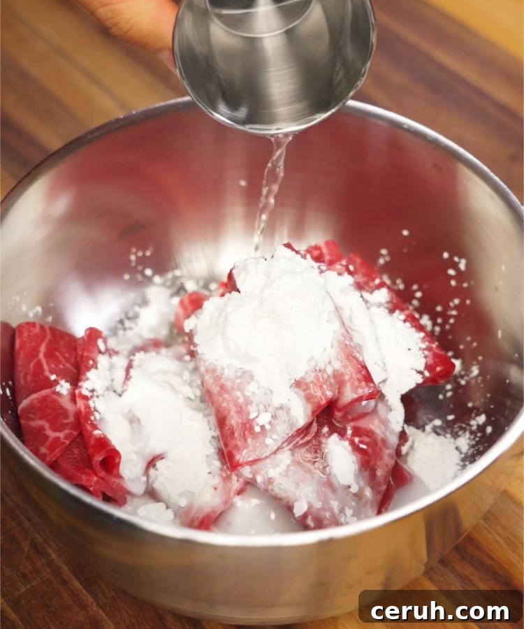 Beef slices being evenly coated in a cornstarch slurry inside a metal mixing bowl, preparing the meat for quick stir-frying. This method enhances the texture and ensures the beef stays tender in the final Beef Lo Mein dish.
