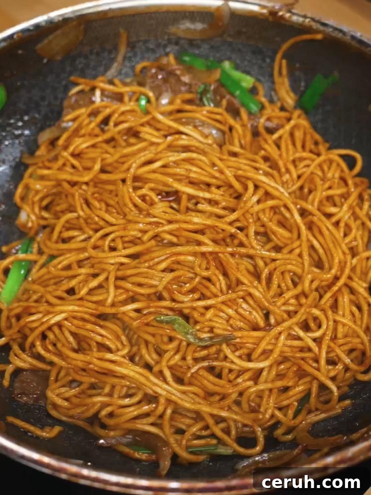 Beef Lo Mein noodles being tossed in the marinated beef, sauce, onions, and green onions after being tossed very well until all ingredients are tossed well like a Chinese takeout dish.