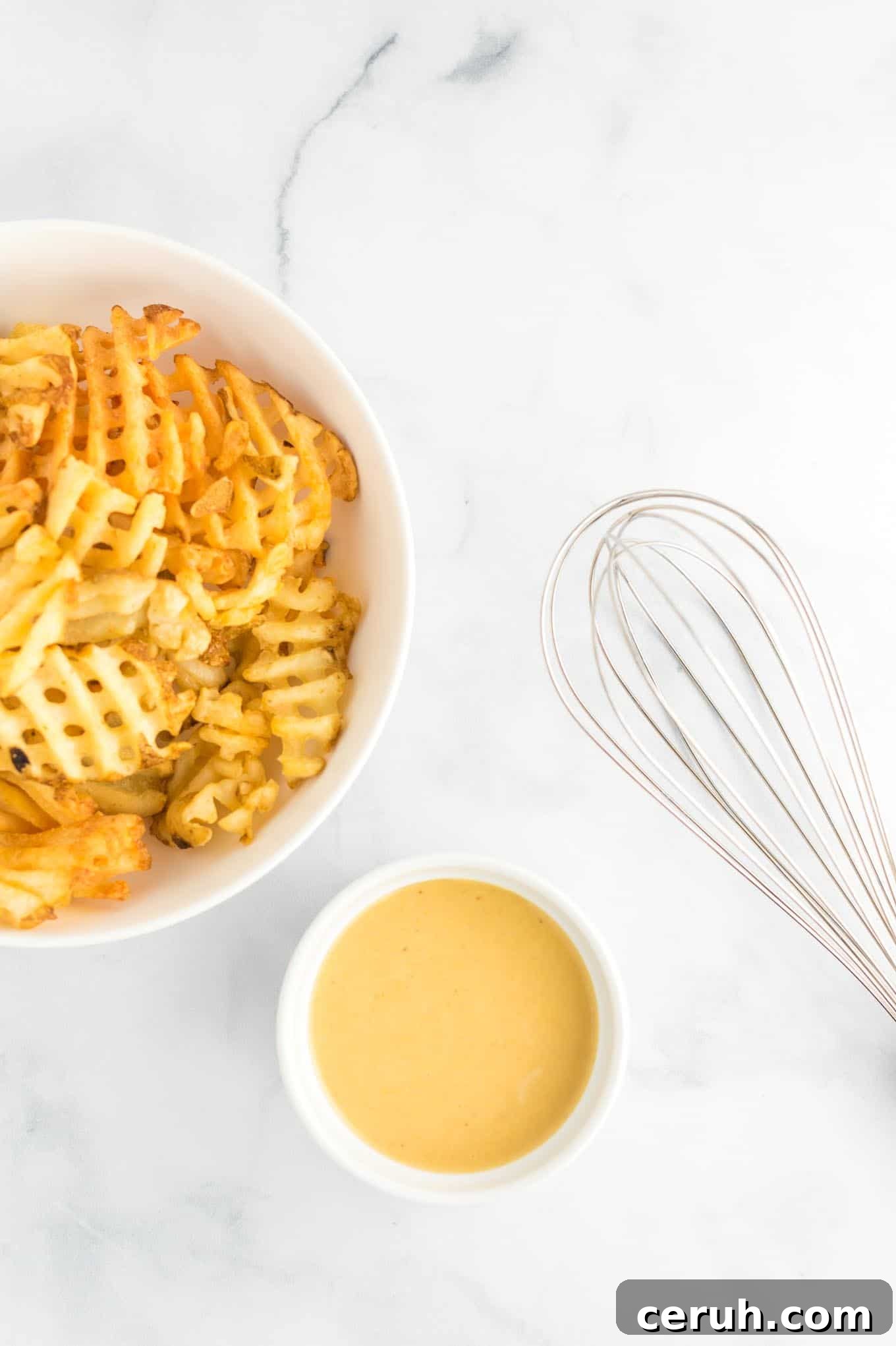 sauce in a white ramekin with fries in a bowl and a whisk