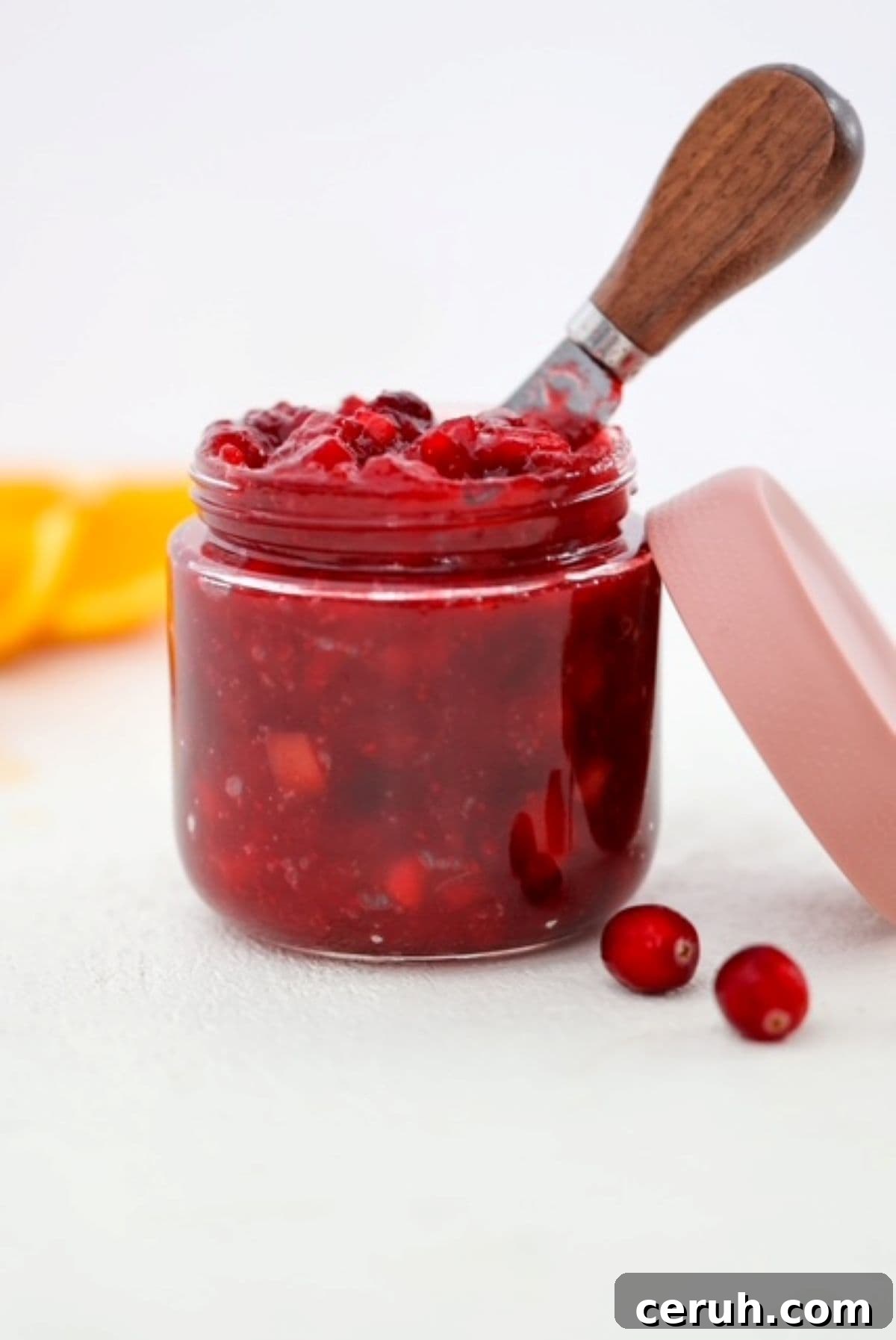 Cranberry sauce in a glass jar with the lid and a few cranberries the side.
