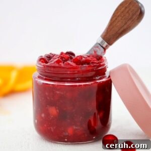 Homemade low sugar cranberry sauce in a glass jar, with the lid and a few cranberries to the side.