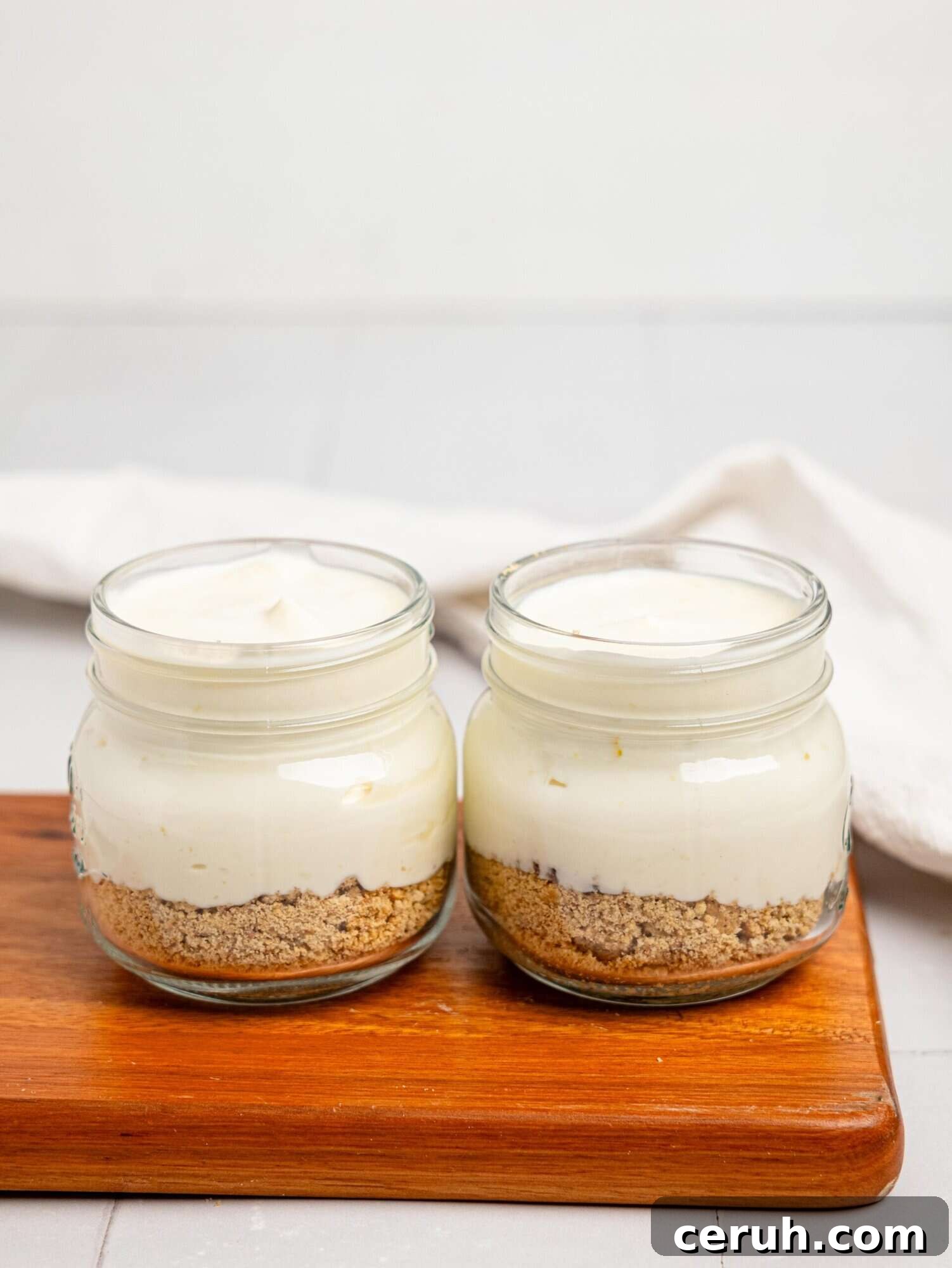 Crushed biscuits and lemon cheesecake filling in two jars.