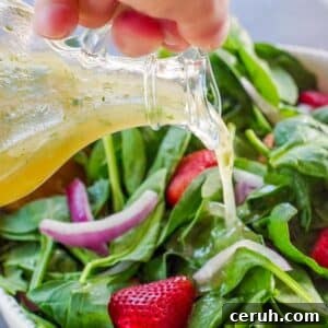 honey lime cilantro vinaigrette being poured over a strawberry spinach salad