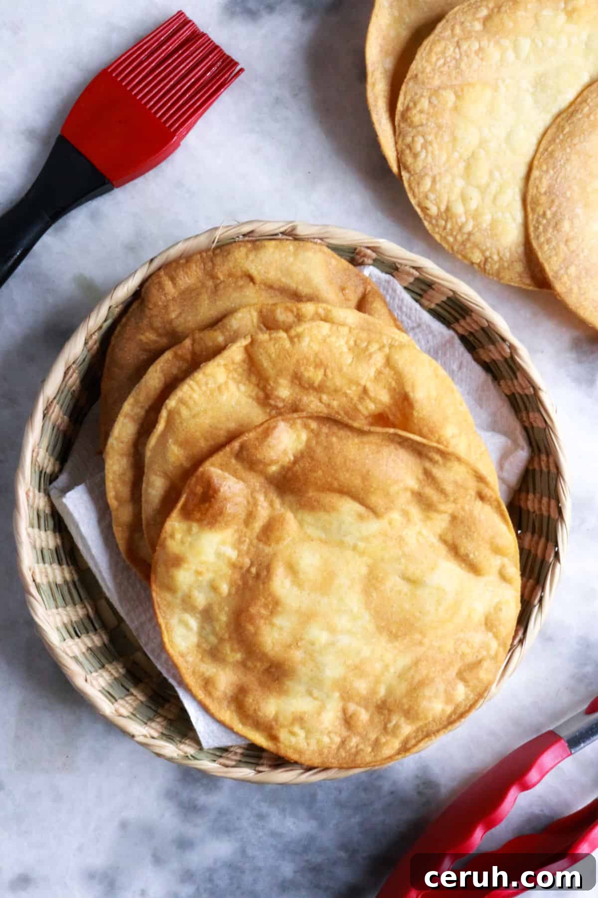 Homemade Tostada Shells: Crispy Tortilla Shell Recipe 10 Tostada shells on a white surface with a pastry brush and tongs