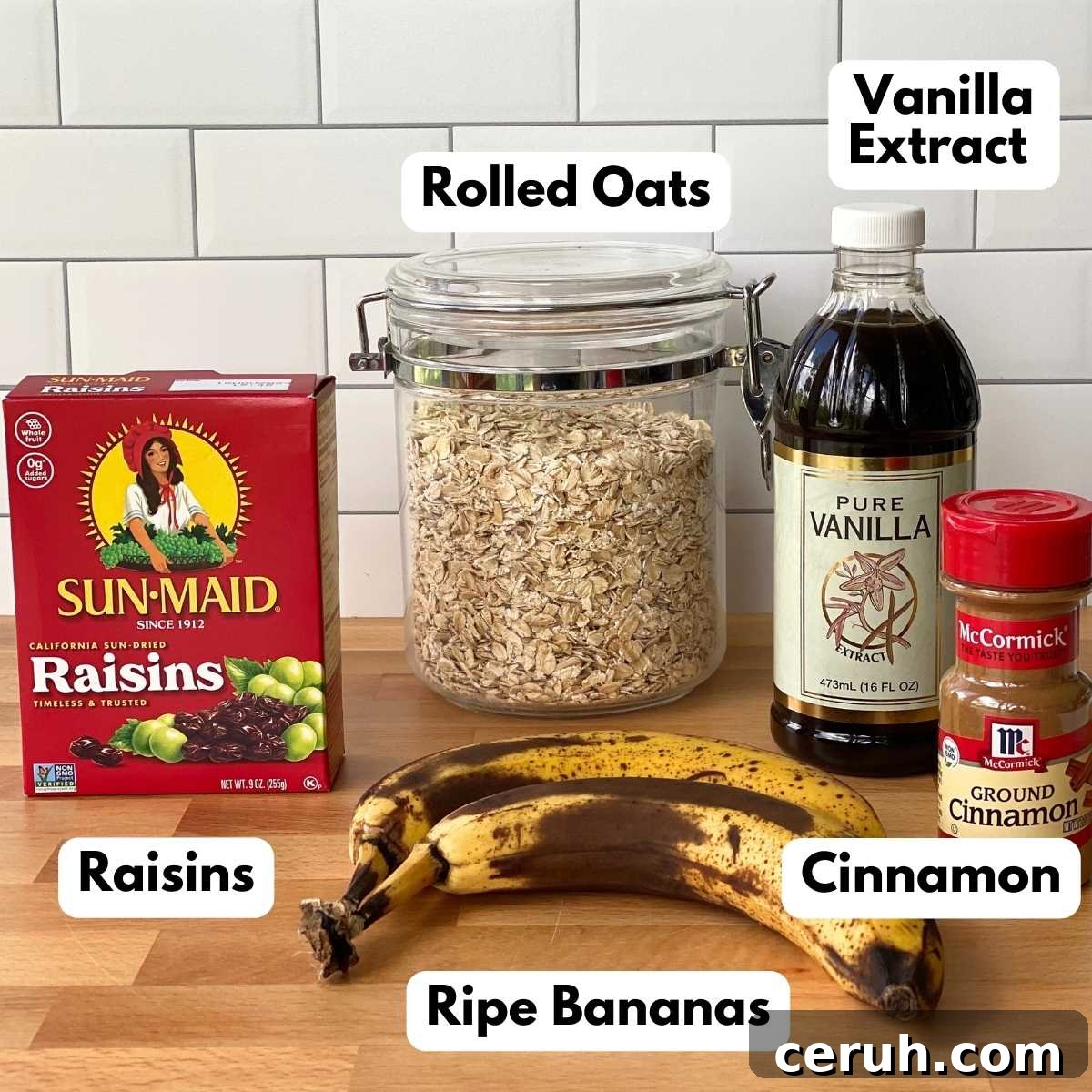Canister of oatmeal, box of raisins, vanilla extract, bottle of cinnamon and 2 ripe bananas on a countertop.