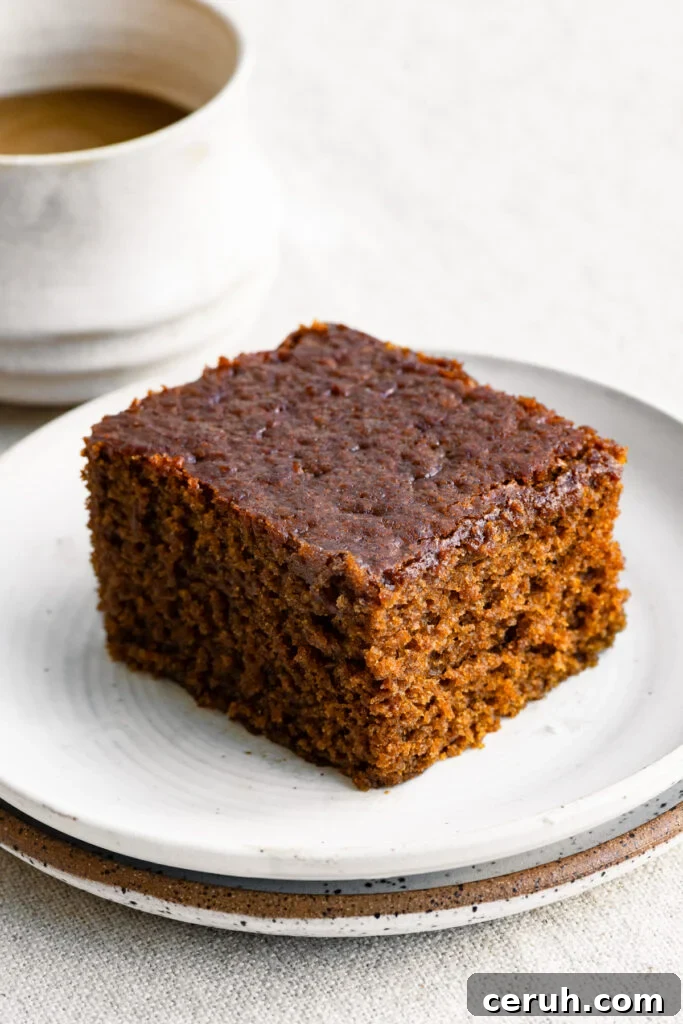 Slice of gingerbread cake on a plate next to a cup of coffee.