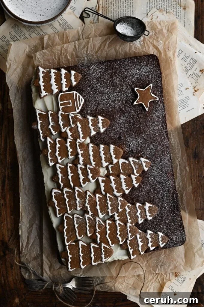 Gingerbread sheet cake topped with Christmas tree shaped cookies on wood table.