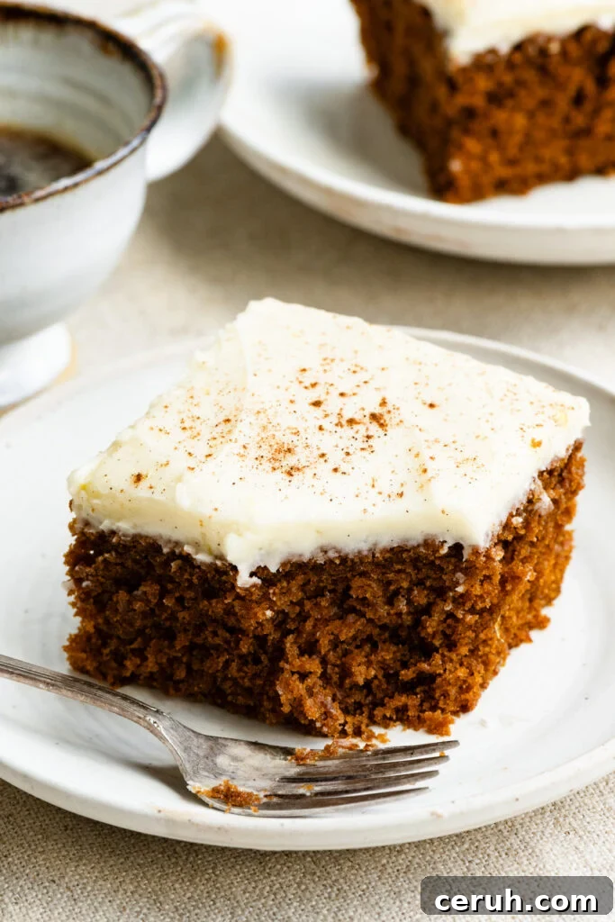 Slice of gingerbread cake topped with frosting on a plate with a fork and a bite missing out of it