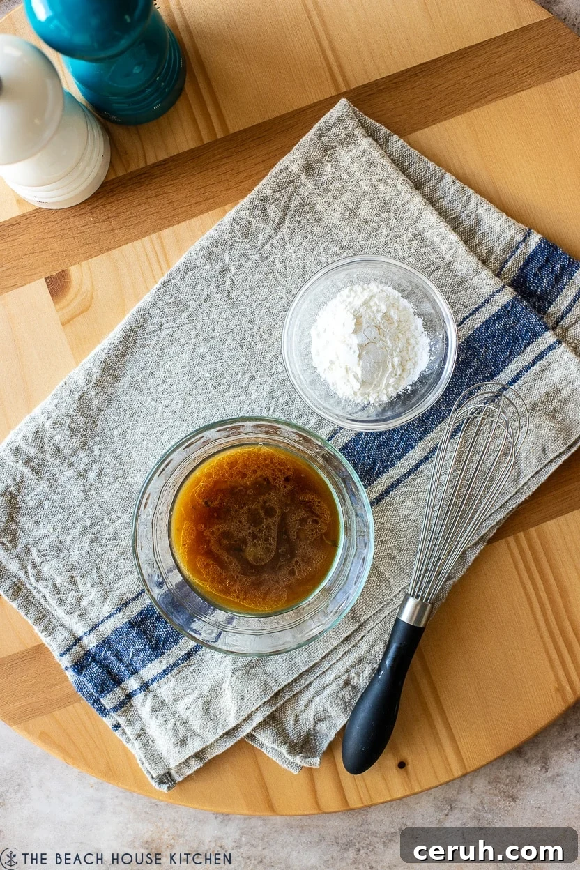 Overhead photo of a small bowl of beef gravy, a small bowl of cornstarch and a whisk