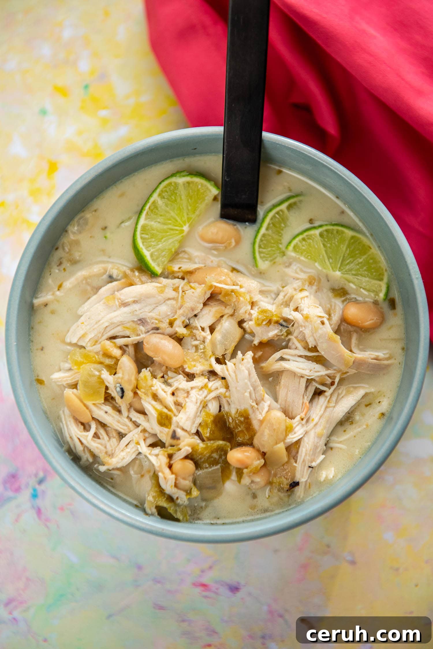 blue bowl filled with shredded chicken in white chicken chili topped with sliced limes