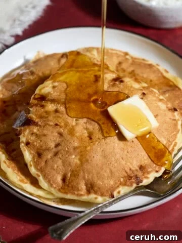 A stack of Sourdough Protein Pancakes with syrup pouring on top.