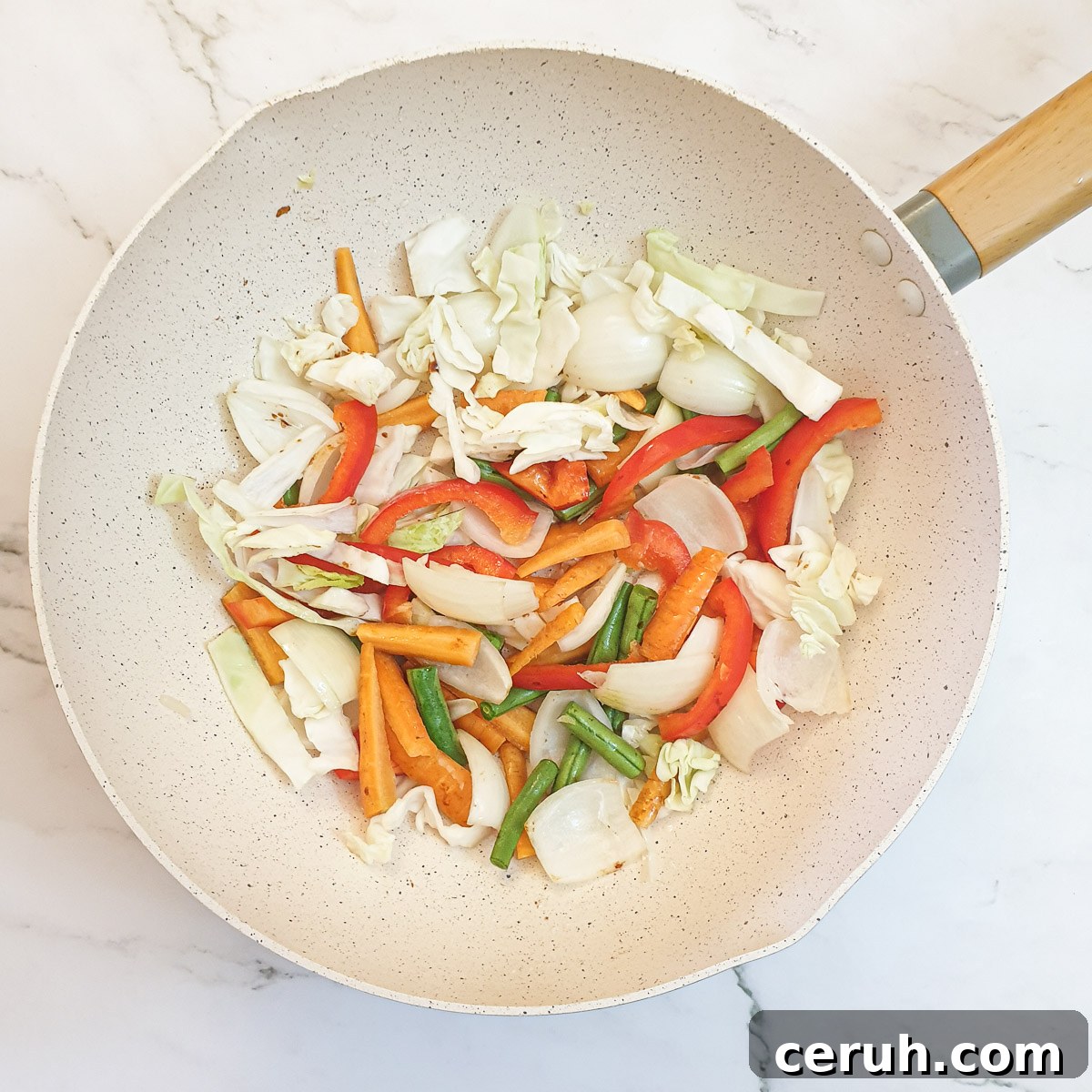 Sliced cabbage, red peppers, onions, carrots and green beans in a frying pan.