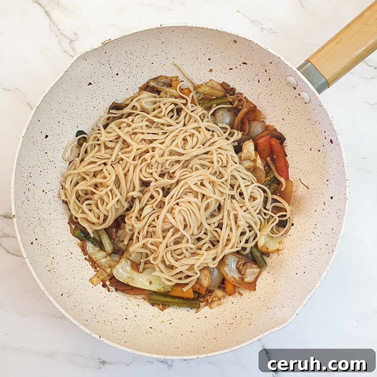 Cooked noodles being added to the vegetable lo mein.
