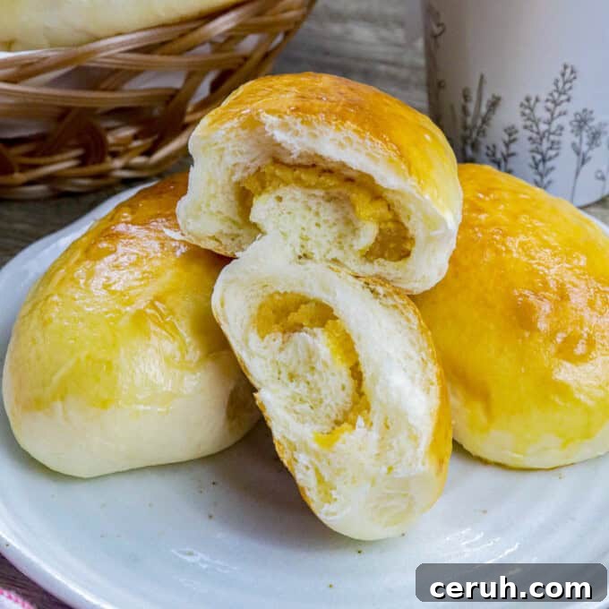 Filipino custard buns on a white plate with a basket of bread rolls and cup of coffee in the background.
