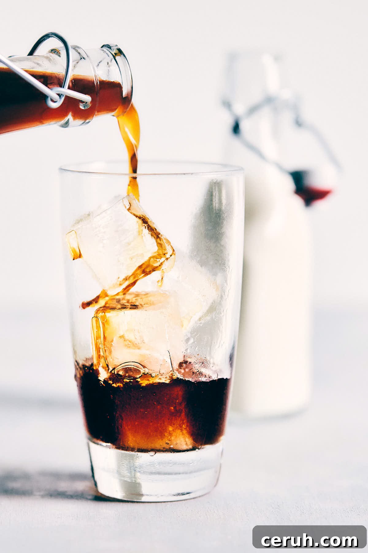 Cold brew coffee being poured over ice in a glass with cream in the background
