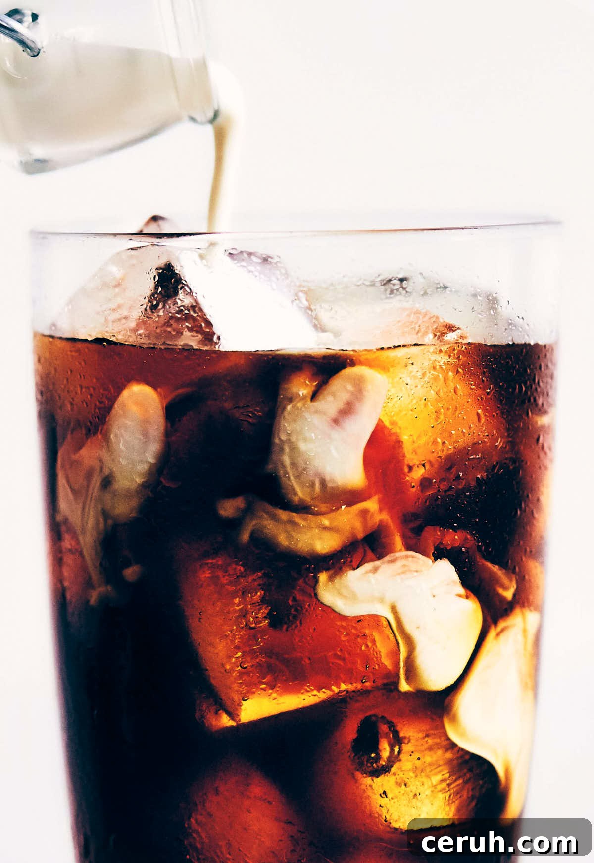 Cream being poured into a glass of cold brew coffee