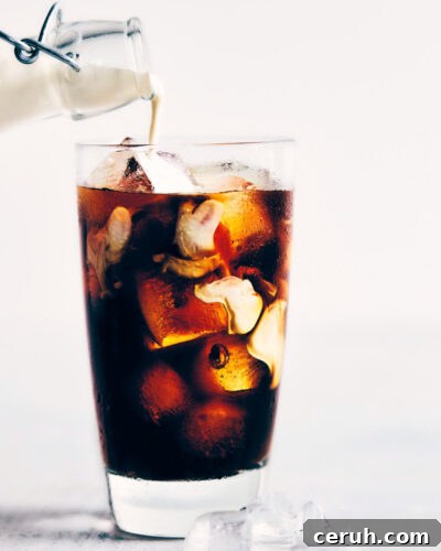 Cream being poured into a glass of cold brew coffee