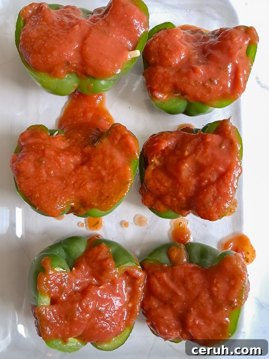 green bell peppers stuffed with ground beef and rice mixture and covered in sauce, ready to bake.