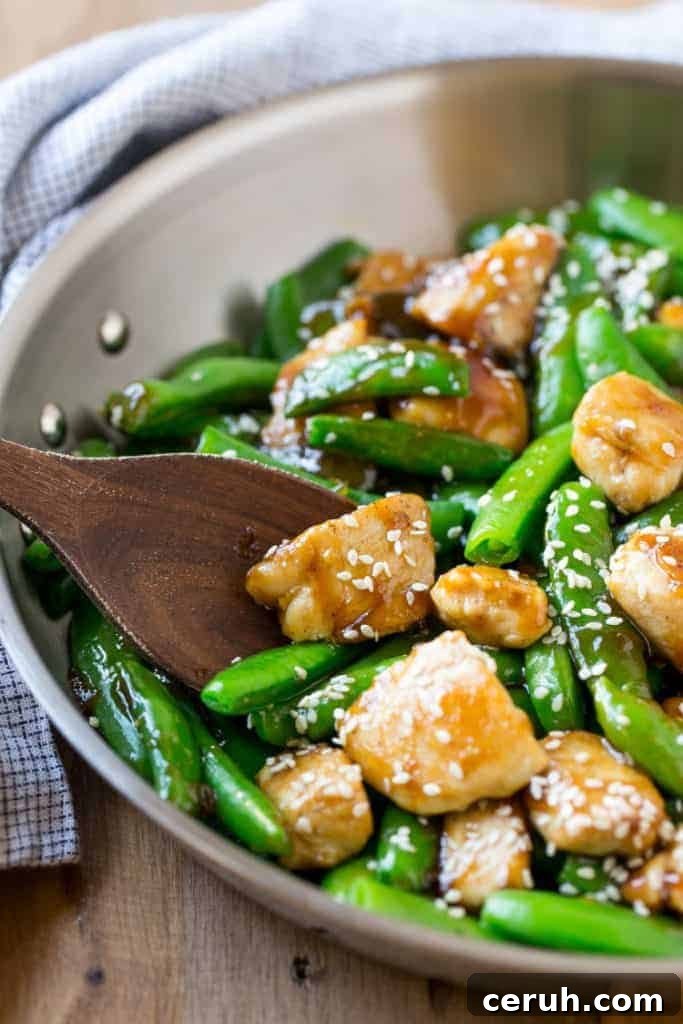 wooden spoon in a pan that has stir-fried chicken bites with green snap peas