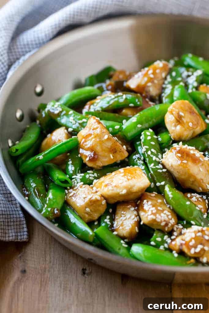 side shot of a pan with chicken and veggies stir fry recipe topped with sesame seeds