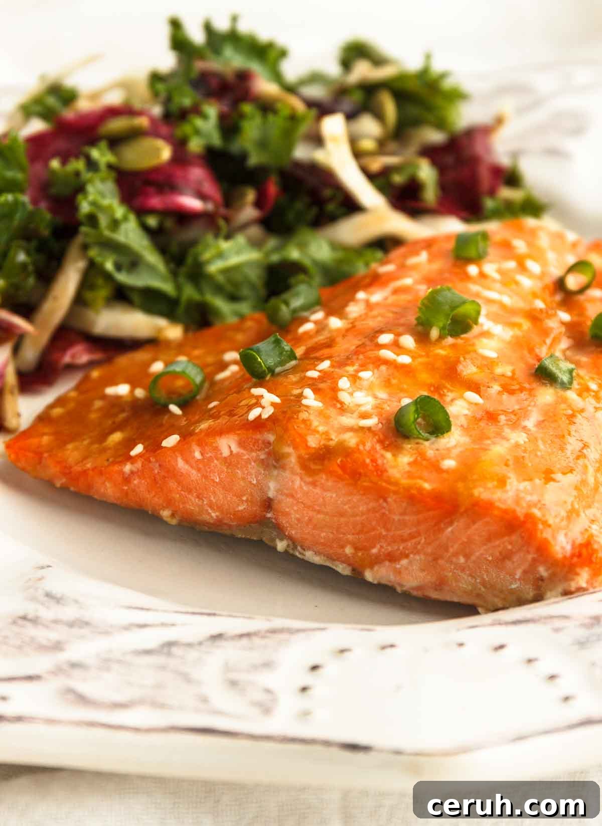 Apricot glazed salmon on a white plate with salad.