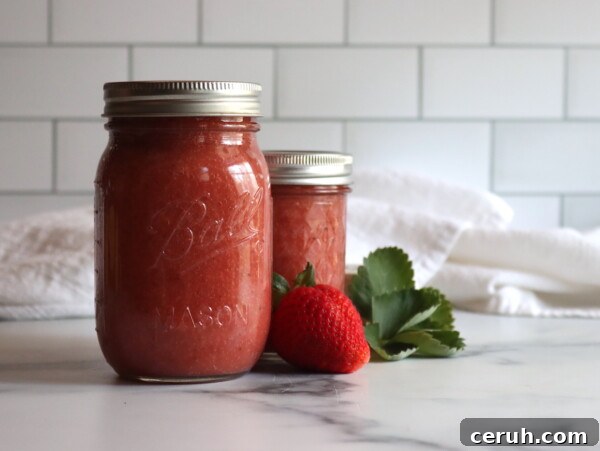 Strawberry Applesauce in a pint and half pint jar on a white table with strawberries next to it.