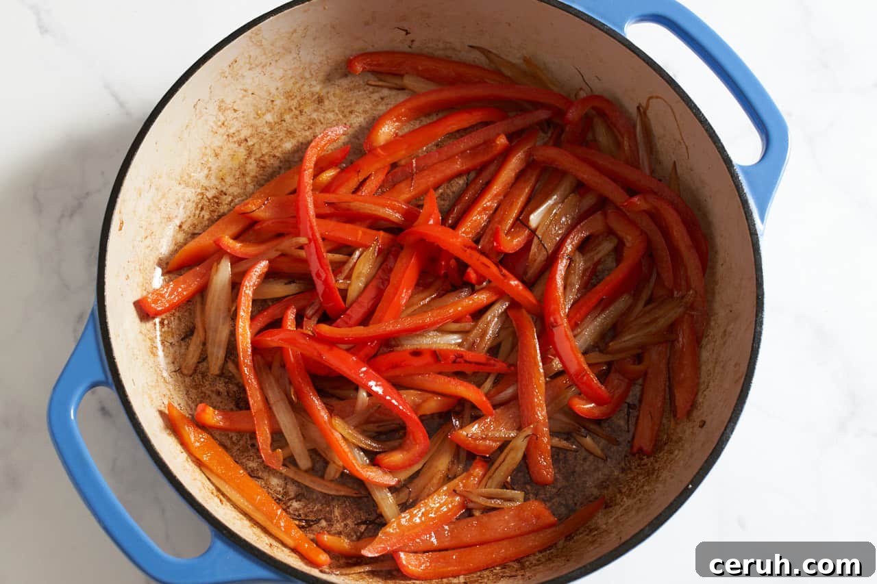 Sautéed red bell peppers and onions in a blue pan.