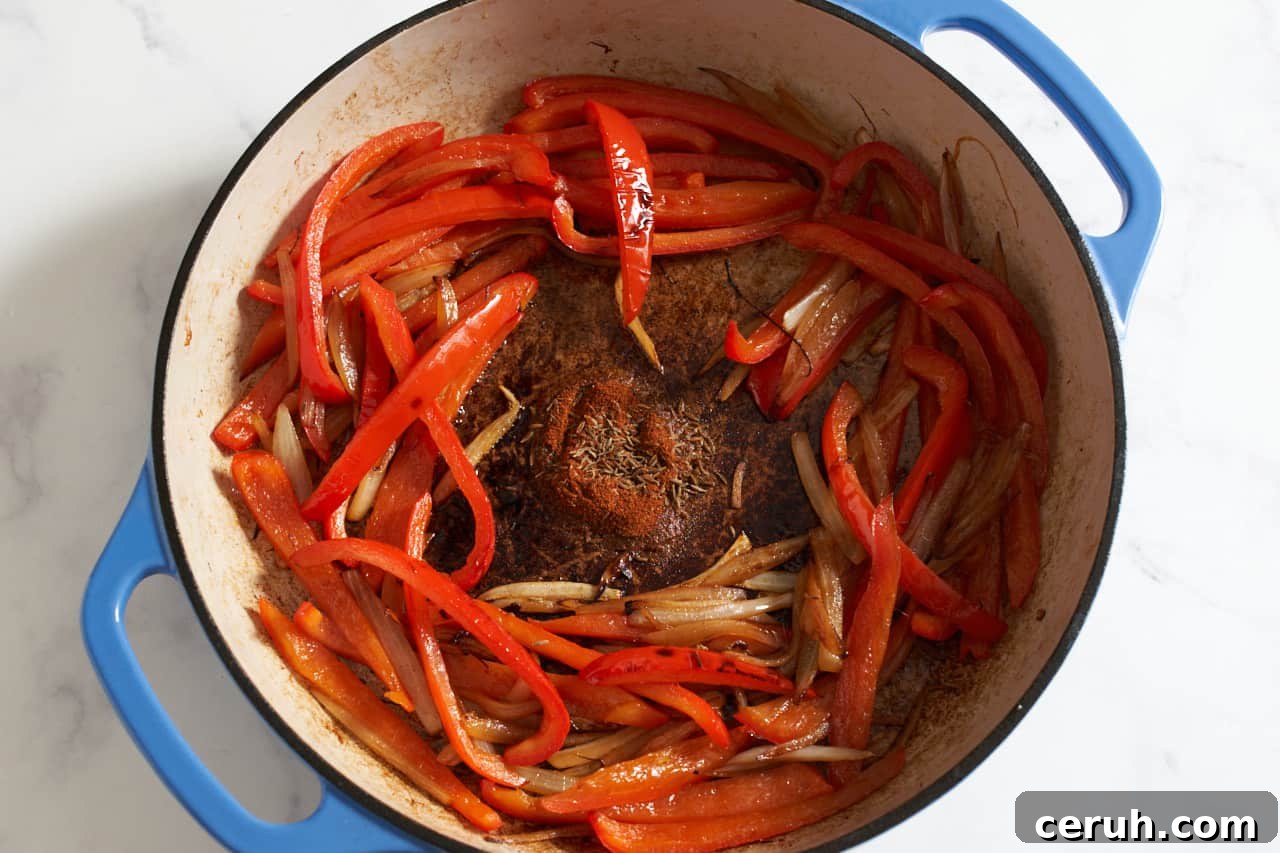 Sautéed red bell peppers and onions in a blue pan with paprika and cumin seed blooming in the center.