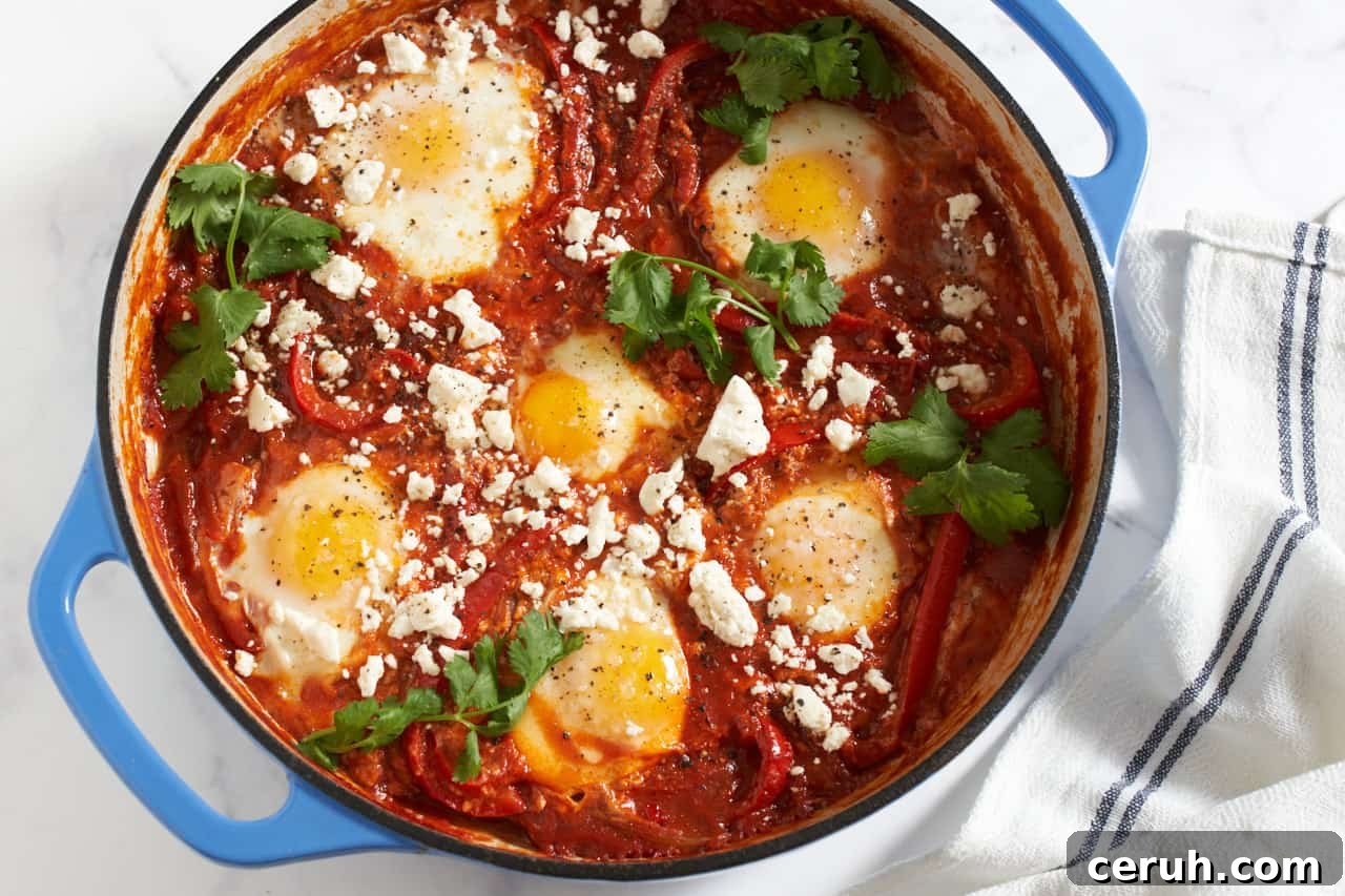Shakshuka with feta and cilantro in a blue pan with a blue and white striped towel next to it.